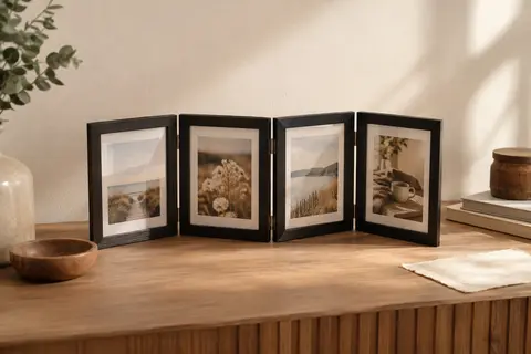 Cadre photo pliable noir à quatre ouvertures, posé sur une console devant un mur crème
