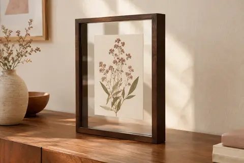 Cadre photo flottant marron posé sur une console, avec une image botanique visible entre deux vitres.