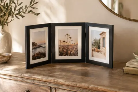 Cadre photo pliant noir à trois vues posé sur une console en bois dans un intérieur lumineux aux murs crème.