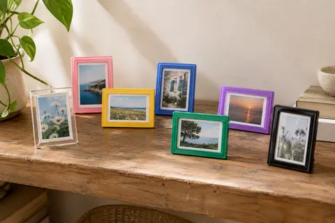 Sept mini cadres photo colorés à poser, exposés avec des tirages instantanés sur une étagère en bois.