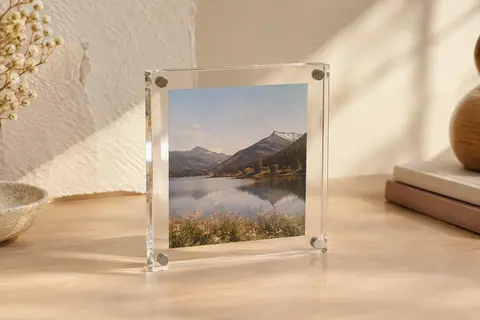 Petit cadre photo transparent en acrylique, fermé par des aimants aux quatre coins et posé sur un bureau clair.