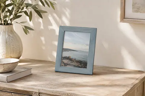 Cadre photo gris azur texturé posé sur une console contre un mur crème, avec une image de paysage.