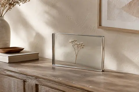Cadre photo flottant en métal argenté et verre, posé sur une console en bois avec une fleur séchée