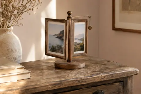 Cadre photo rotatif en bois avec deux vues et un petit pendentif cœur, posé sur une console claire.