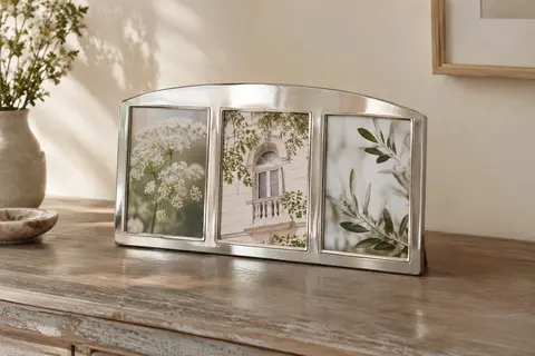 Cadre photo triple argenté à profil miroir posé sur une console en bois devant un mur crème.