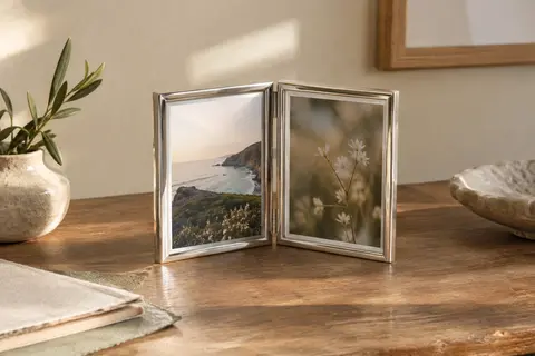 Petit cadre photo double articulé en métal argenté, posé avec deux portraits sur une table en bois.